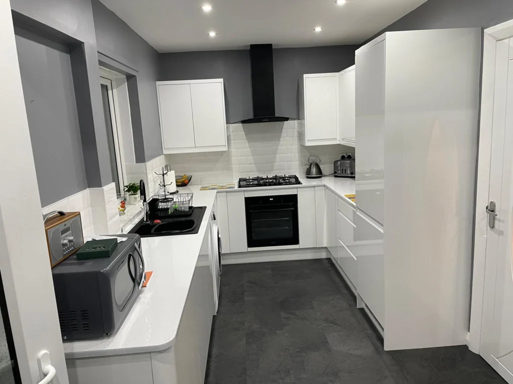 Modern kitchen with white units, a grey feature wall and dark tiled flooring